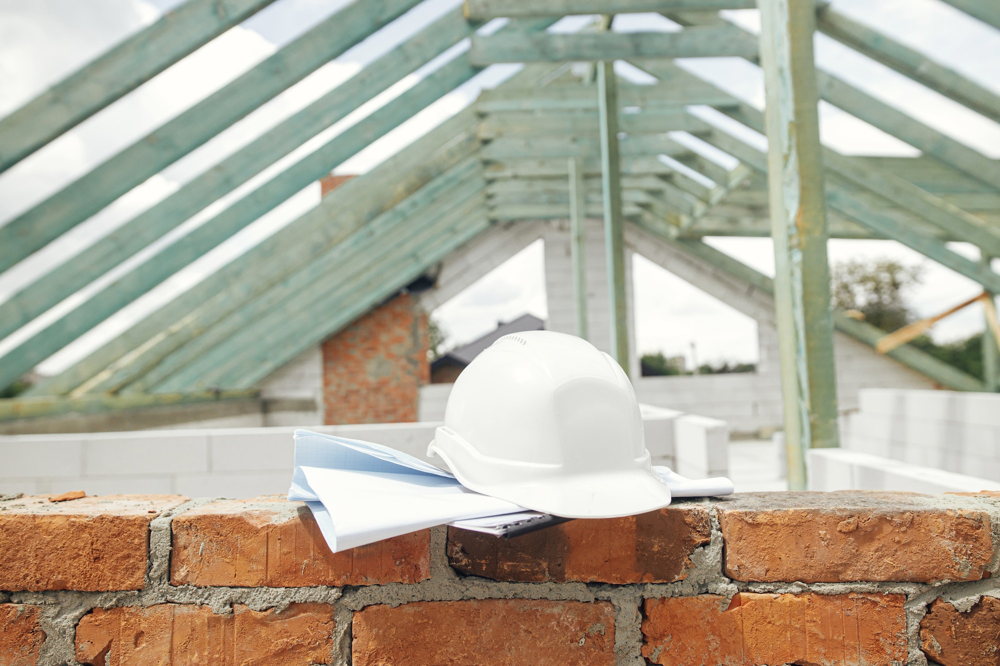 Hard hat with house blueprints on brick masonry at wooden roof framing. Architecture. House building